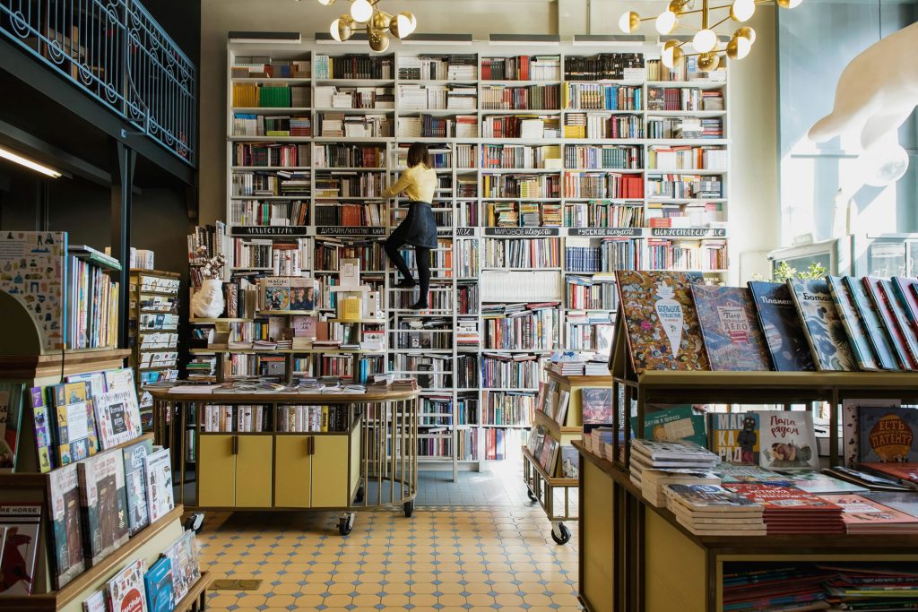 A lady standing on a ladder next to a bookcase in a book store